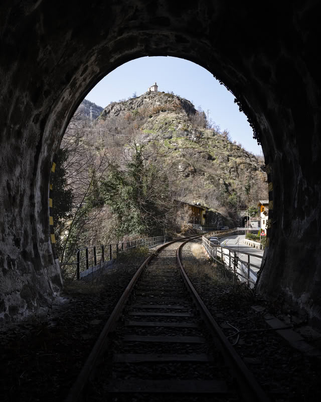 Railway track emerging from a tunnel, with a chapel above